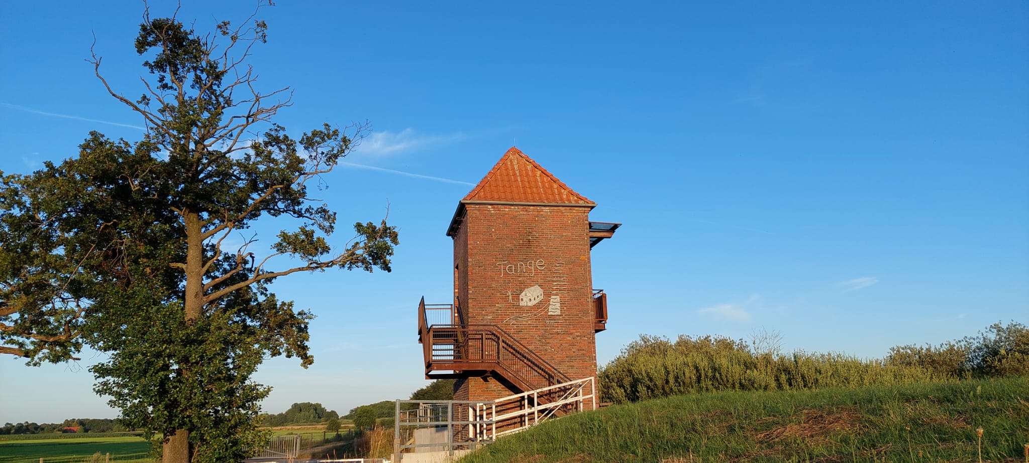 Der Tange-Turm im Abendlicht mit Blick auf Wiesen und Kanal